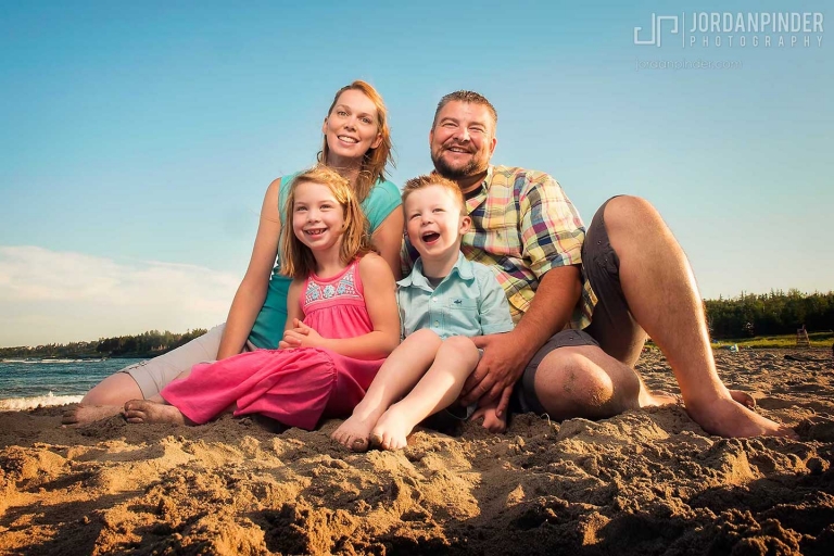 family of four sitting on beach smiling