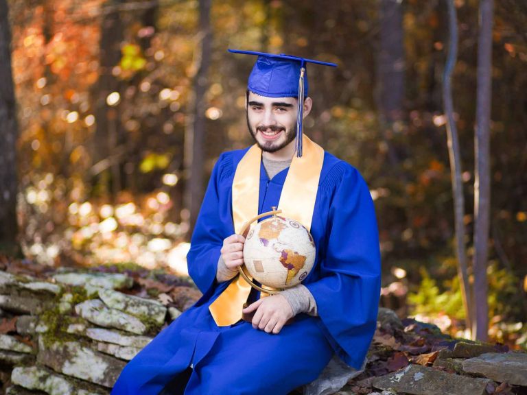 high school graduate sitting on rocks in gown holding globe