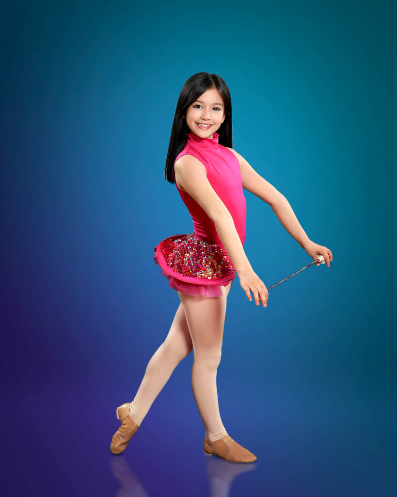 girl holding baton posing in front of blue backdrop